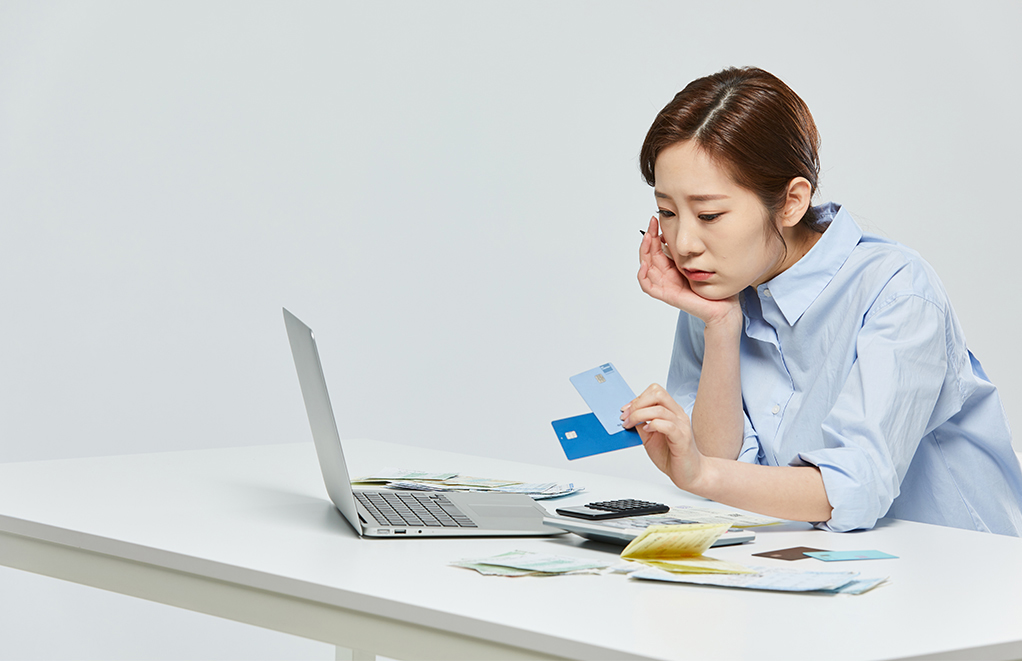 여성이 신용카드를 들고 컴퓨터를 보며 고민하고 있다.