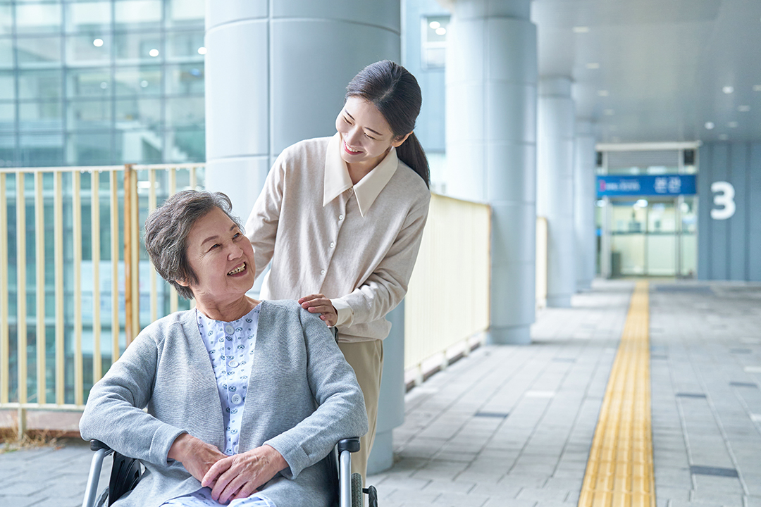 휠체어에 앉은 사람과 옆에서 내려다 보며 웃고 있는 사람 사진