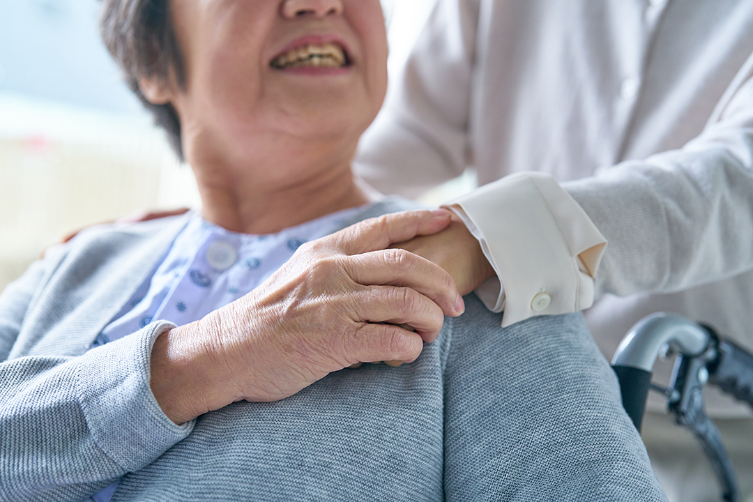휠체어에 앉은 사람과 옆에서 손을 잡고 있는 사람 사진