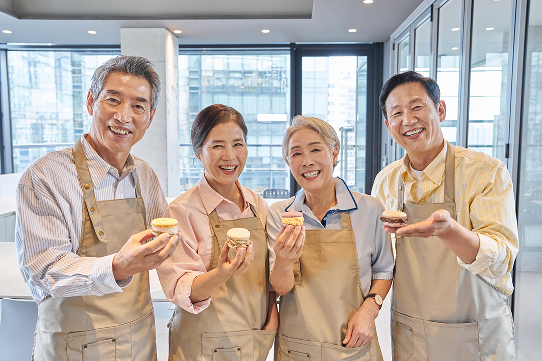 앞치마를 입은 네 사람이 주방에서 디저트를 들고 웃고 있는 모습